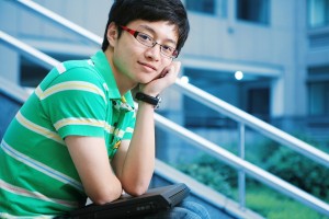 Asian male college student on campus steps thinking